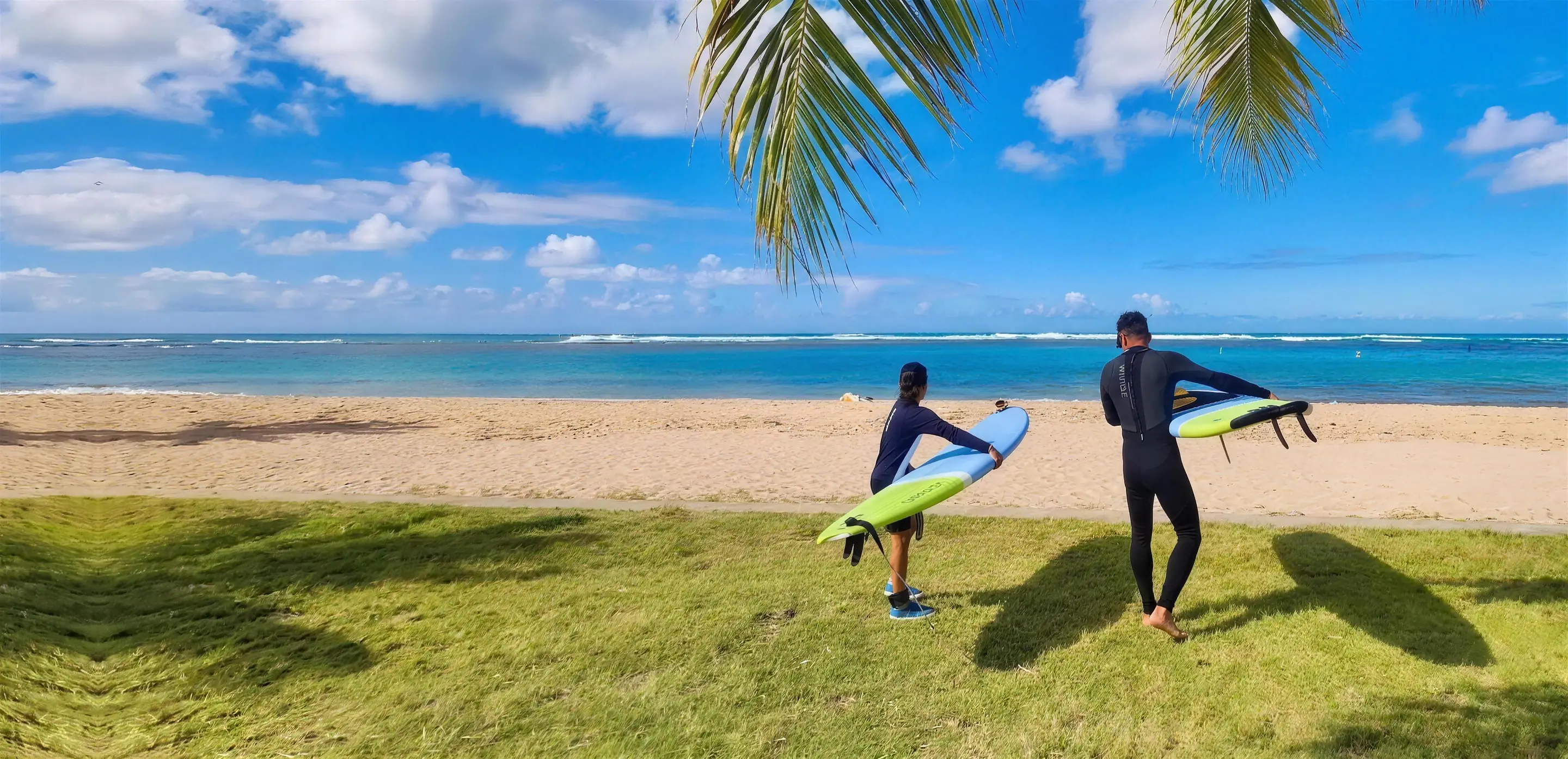 A child and an instructor carrying a surfboard toward the ocean under palm fronds