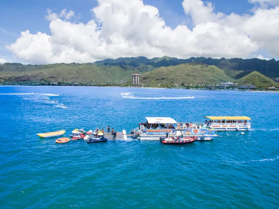 Jet skis, a banana boat and a tour boat lined up at a platform on Maunalua Bay